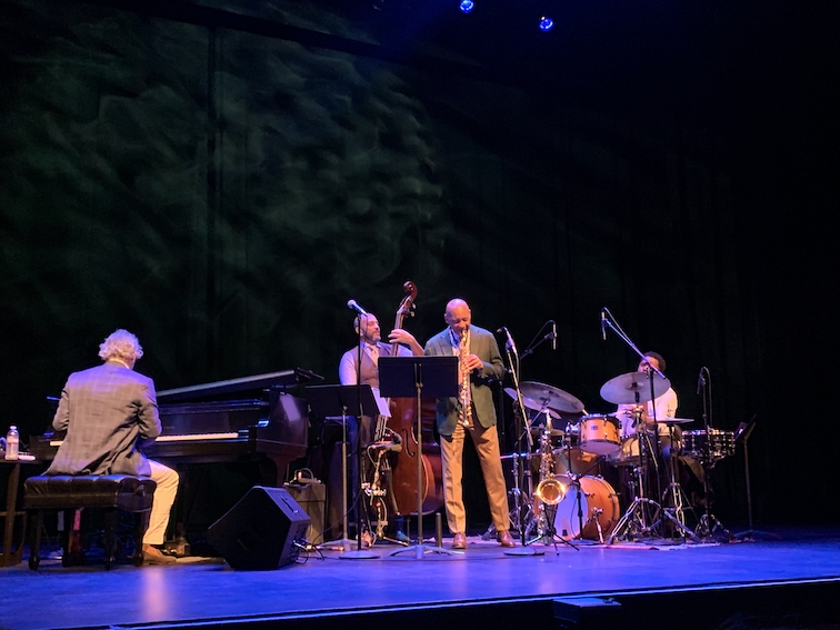 Branford Marsalis quartet (piano, Branford on sax, bass, drums) performing on a darkened stage