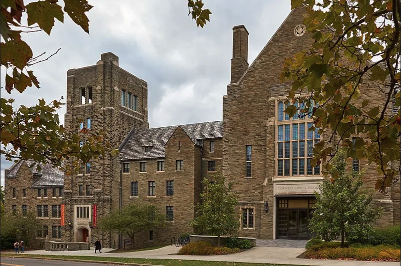 One side of a large, rambling, multi-story, multi-level, stone building, with pitched roof, chimeys, a tower, and a main portion that exceeds the height of the other portions