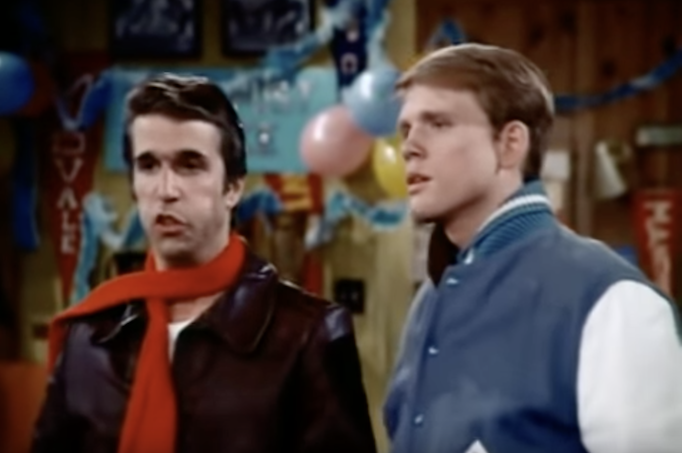 Fonzie, a cool kid in a black leather jacket, struggling to speak to his friend Richie Cunningham, dressed in his high school varsity jacket