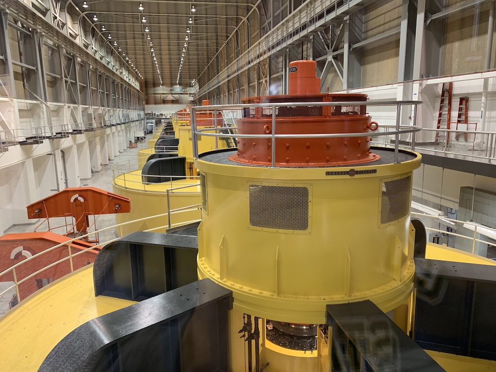 A very large, completely enclosed industrial room, with eight or so huge circular pieces of machinery on the concrete floor painted yellow, red, and black