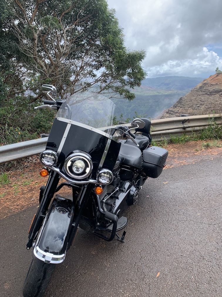 A black motorcycle parked at the side of the road above a deep canyon with exposed rock and vegetation