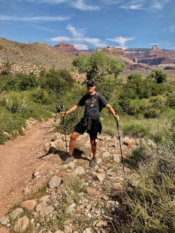Chris Shaver holding hiking poles while standing on the Bright Angel Trail in Grand Canyon on a bright, sunny day