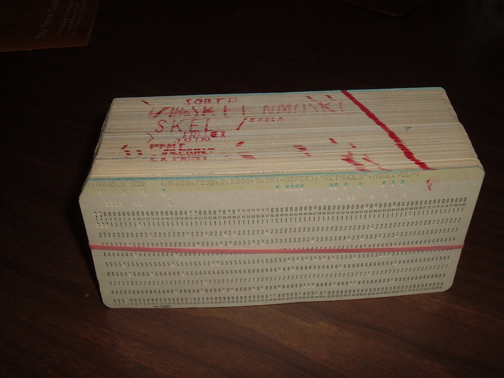 A deck of computer punch cards bound by a rubber band, with writing in red on the side of the deck