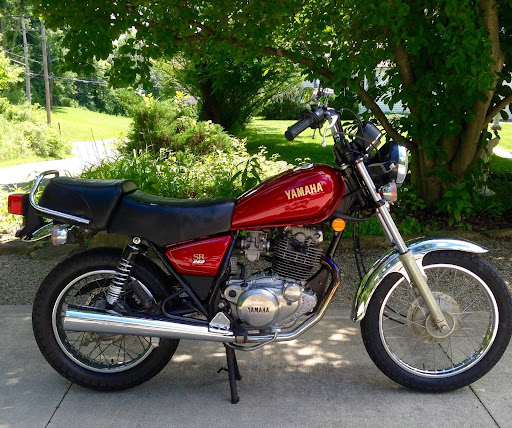 A side view from the right of a red Yamaha SR250 motorcycle with the rearm passenger seat installed
